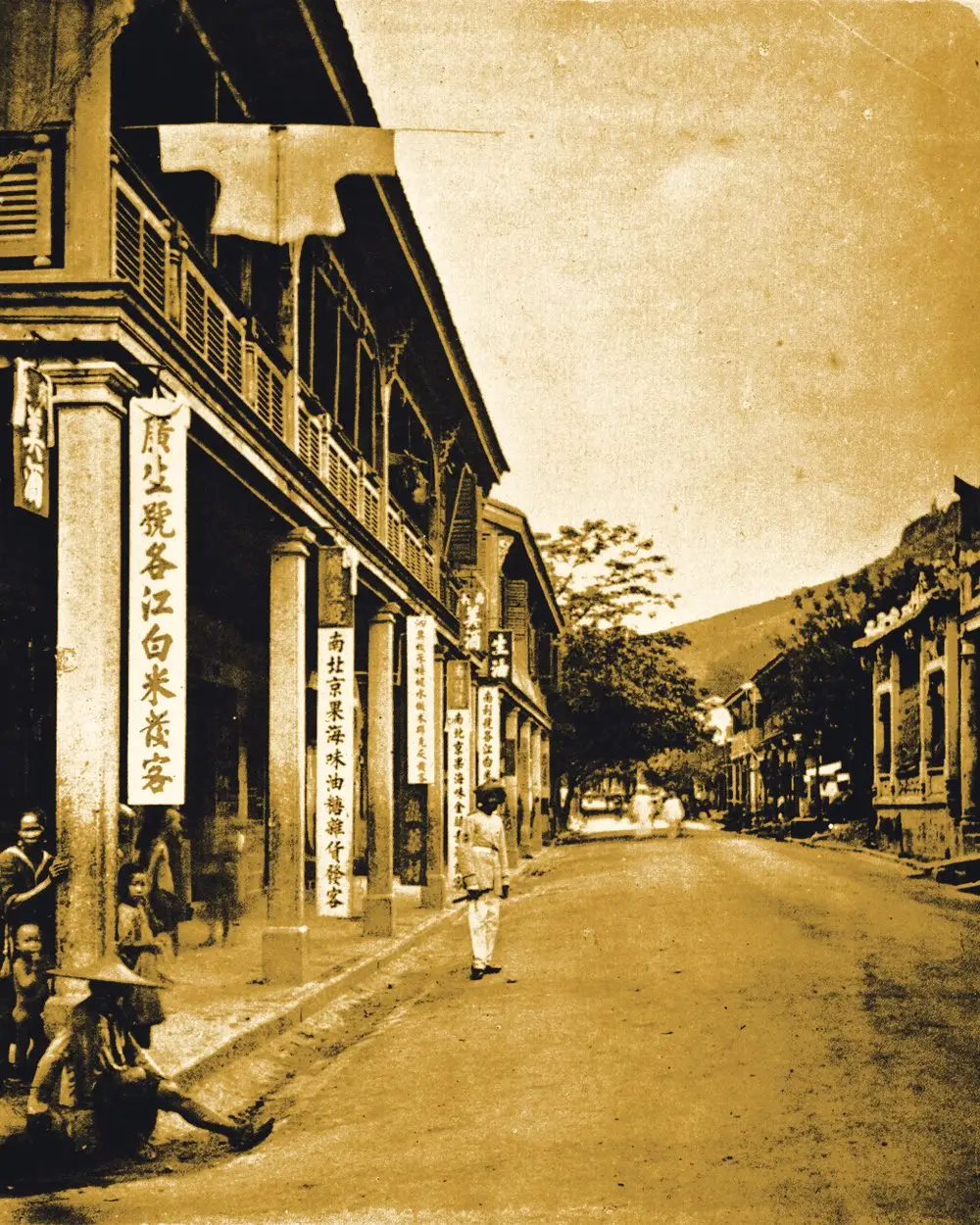 A 19th-century photograph of a Hong Kong street, colonnaded shophouses hung with vertical Chinese signboards